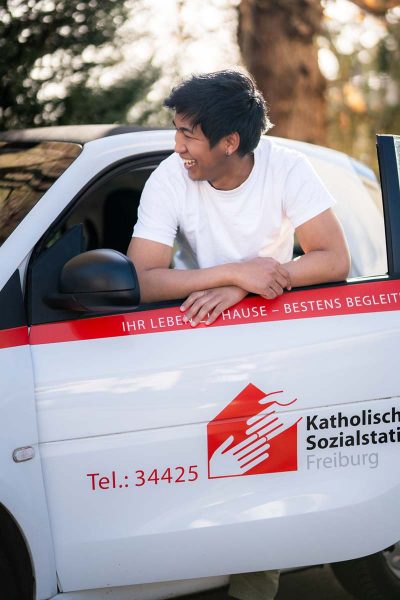 ausbildung-pflegefachkraft-fsj-bfd-01 Freundlicher Azubi / Auszubildender lehnt am Pflegeauto