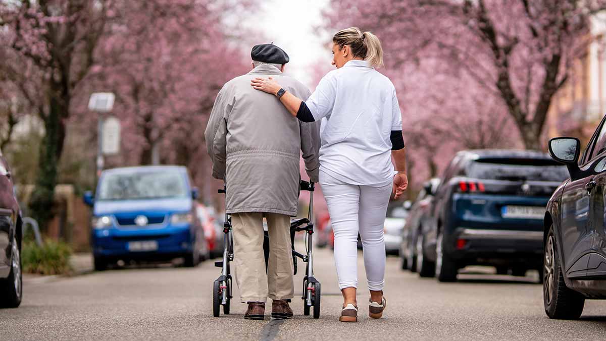 Mitarbeiterin der Nachbarschaftshilfe geht mit einem älteren Herrn spazieren